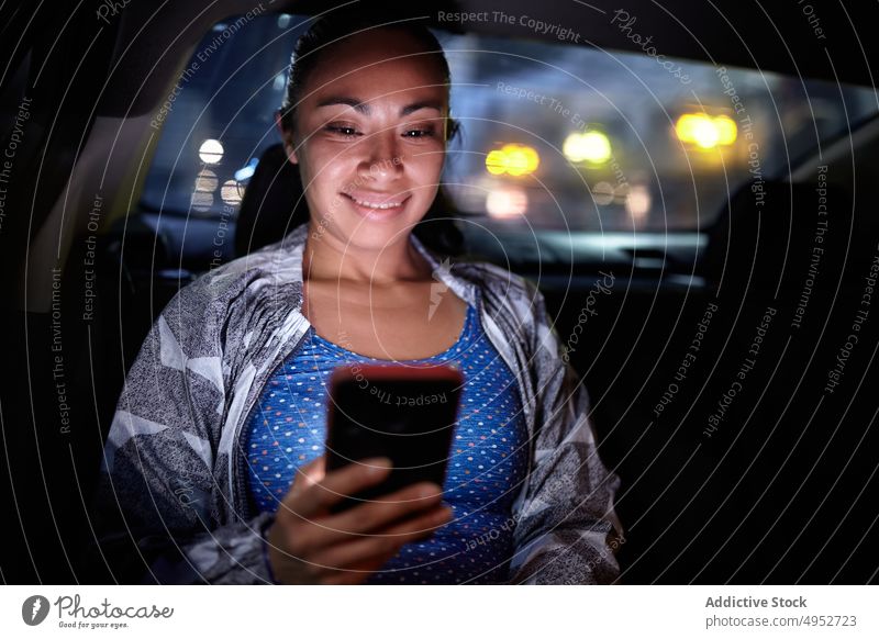 Woman using smartphone in car woman passenger browsing city night automobile female dark cellphone surfing internet message urban backseat device gadget