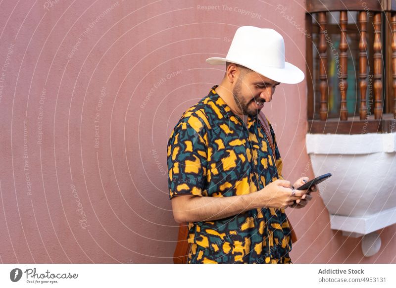 Cheerful man browsing smartphone near building traveler tourist city street trip tourism text message online internet adventure cellphone social media app