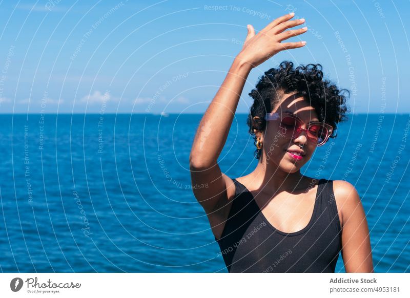 Smiling black woman in sunglasses against endless sea cheerful individuality style tattoo feminine shadow blue sky modern creative design african american