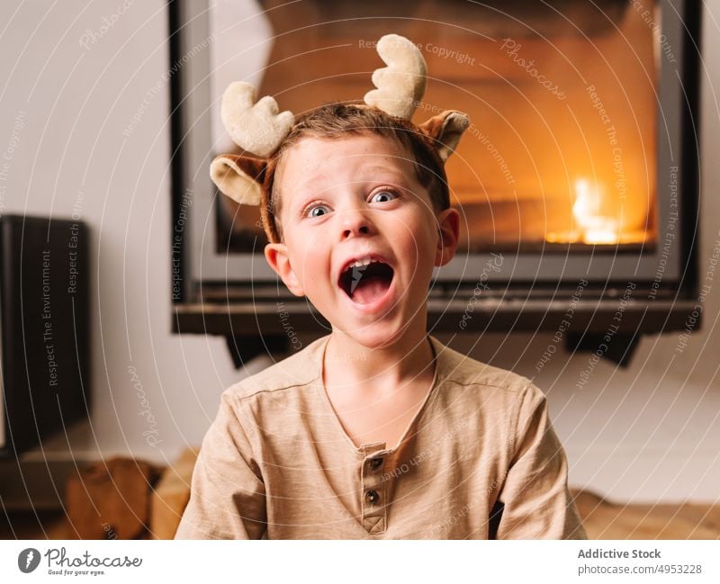 Amazed boy in reindeer antlers near fireplace kid shock headband omg christmas holiday amazed astonish stunning living room surprise wow mouth opened occasion