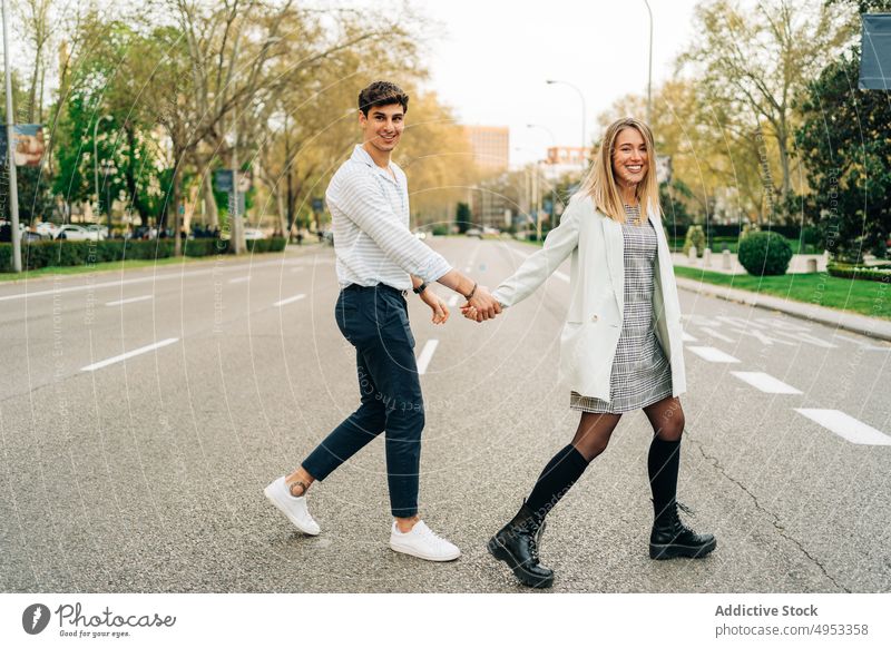 Cheerful couple crossing road in city holding hands walk stroll love together relationship street urban style trendy content smile happy girlfriend boyfriend