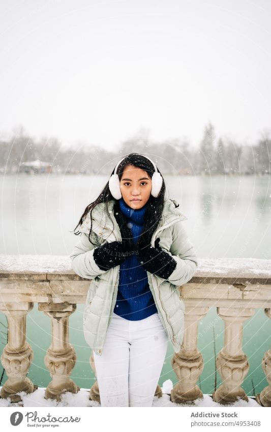 Asian woman under the snow close to lake in winter snowflake admire wintertime river idyllic embankment urban portrait fence old style warm clothes water sky