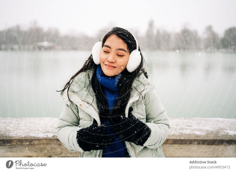 Asian woman under the snow close to lake in winter snowflake admire wintertime river idyllic embankment urban portrait fence old style warm clothes water sky