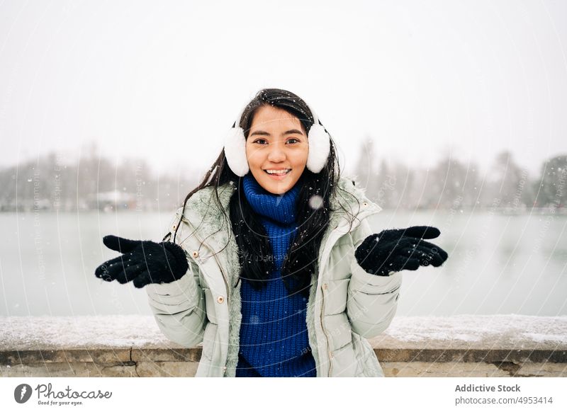 Asian woman catching snowflakes close to lake in winter admire wintertime river idyllic embankment urban portrait fence old style warm clothes water sky enjoy