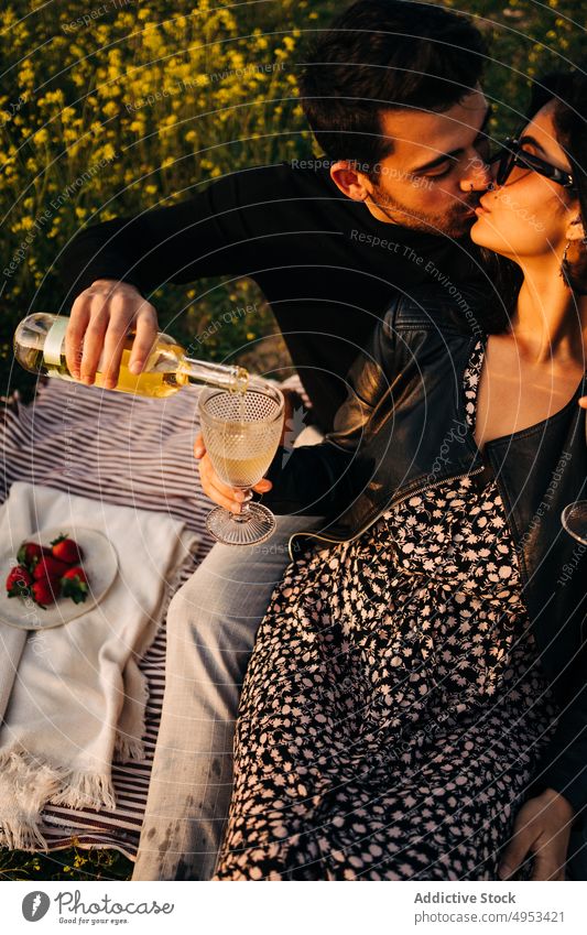 Ethnic couple with bottle of wine on meadow relationship love pour spend time romantic weekend drink beverage alcohol glass bloom flower field sit rest soulmate