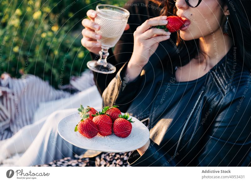 Crop woman eating strawberry against boyfriend on meadow girlfriend drink alcohol spend time weekend delicious lawn couple tasty plate alcoholic beverage glass