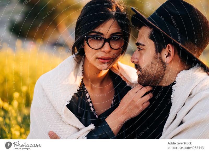 Ethnic woman with boyfriend sitting in field and looking at camera couple spend time weekend romance relationship candid soulmate city plaid eyewear girlfriend
