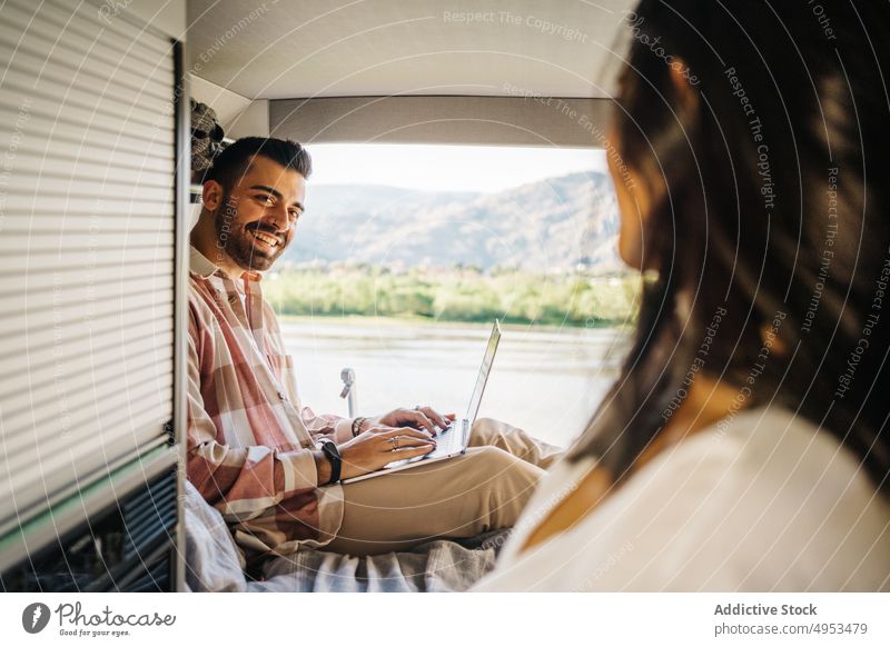 Cheerful ethnic couple of travelers in van camper together cheerful work laptop remote trip hispanic gadget device using boyfriend girlfriend smile vacation