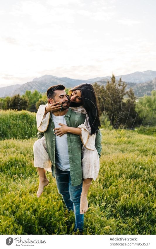 Young couple enjoying summer holidays in countryside piggyback nature together love romantic happy embrace relationship girlfriend boyfriend meadow hill grass