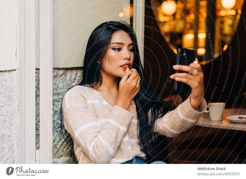 Asian woman with smartphone making up lips in cafe lipstick makeup visage cosmetic beauty feminine windowsill using gadget device decorative product coffee