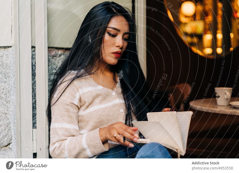 Asian woman writing in notebook on cafe windowsill take note diary attentive feminine millennial charming pen cafeteria focus write denim wear sit concentrate
