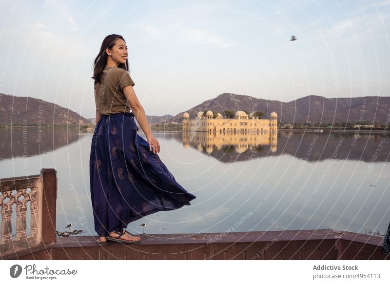 Positive ethnic woman standing near lake and palace tourist visit border water old jal mahal jaipur rajasthan india happy asian smile pond mountain shore coast