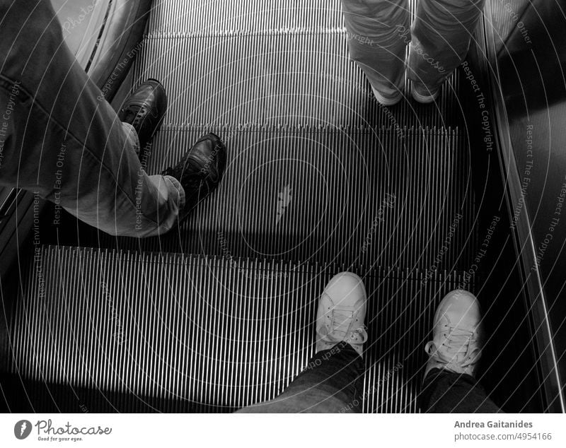 Feet of three people on an escalator, view from above, horizontal Escalator feet Legs Footwear sneakers urban Town Train station Stairs Modern Wait waiting