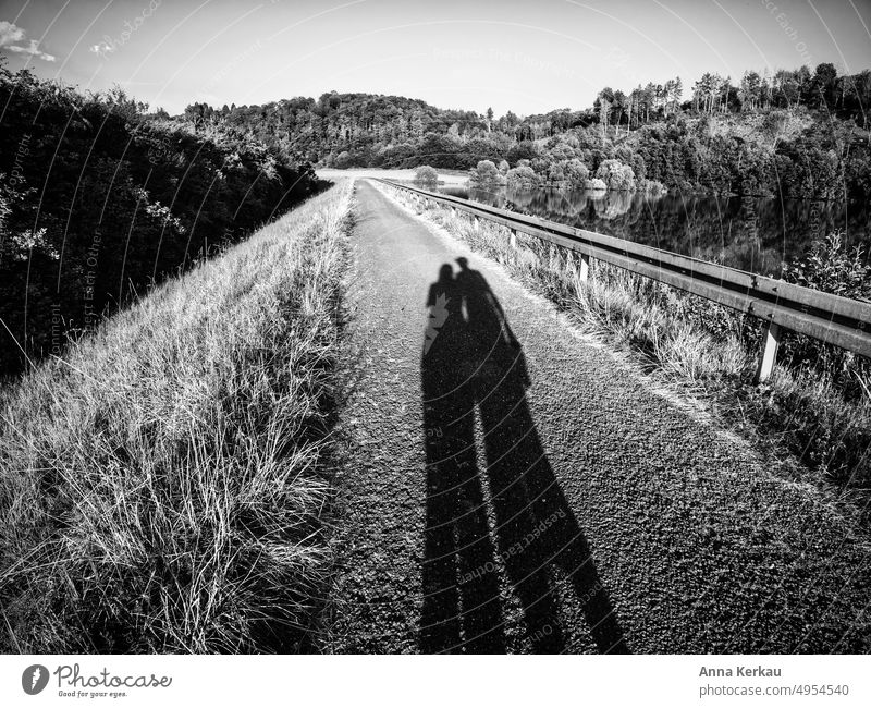 Two long shadows on asphalt path along a lake shore Couple Shadow Silhouette two persons 2 take a walk stroll Light and shadow Attachment Relationship In pairs