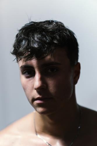 Close-up of a teenager with a serious expression, dark eyes, sweaty skin and contrasted light from above close-up adolescent intrigue mystery shadow wet