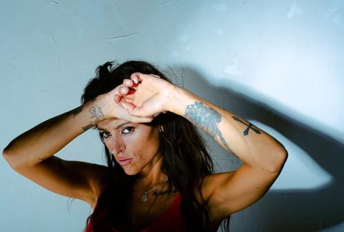 Young tattooed Latina girl with a hard expression and hands crossed on her forehead protects herself from intense light. young latina crossed hands hard shadow