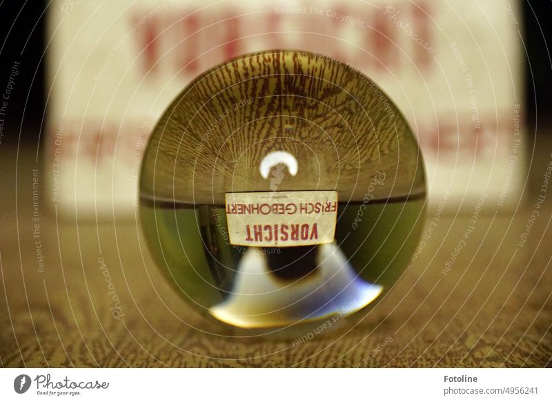 A glass ball is lying on the floor. In it you can see upside down the sign on which "CAUTION FRESH BONED". Glass ball Sphere Round Reflection Colour photo Light