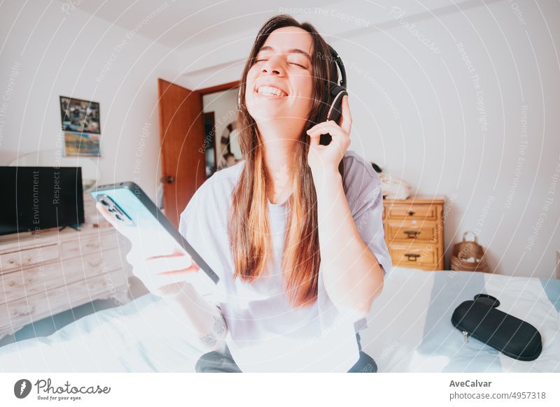 Happy and enthusiastic woman enjoying life, listening to music or favorite podcast with mobile phone and wireless headphones in bedroom. Free time leisure activities, young people new way of streaming