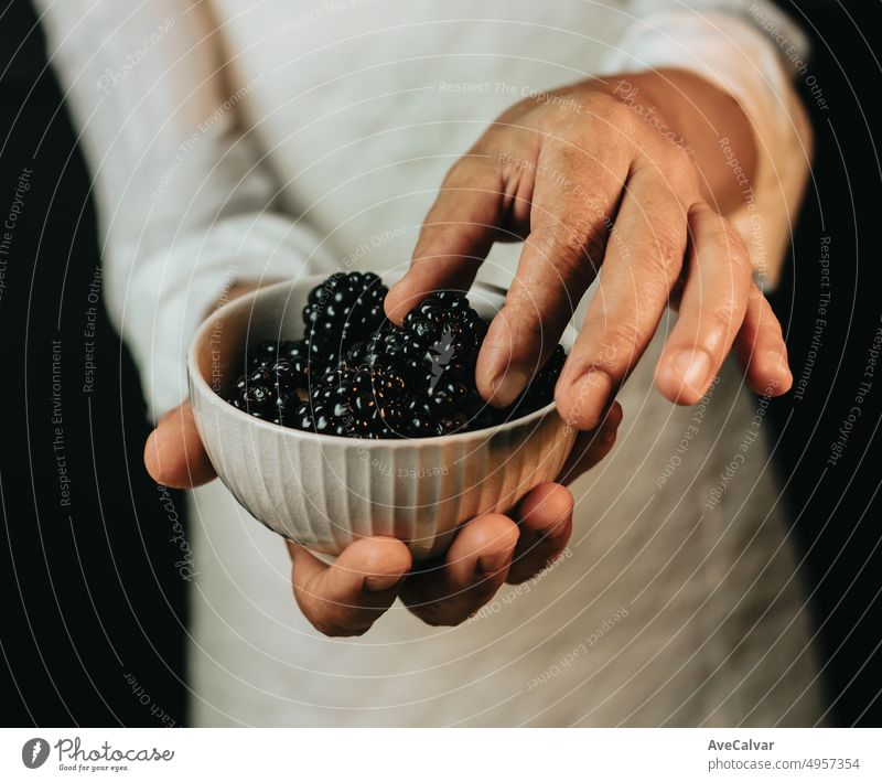 Close up of hands holding a bowl with blackberry showing the necessary amount to make the recipe of a dessert.Preparing a healthy and sweet meal suitable for breakfast,brunch or afternoon snack
