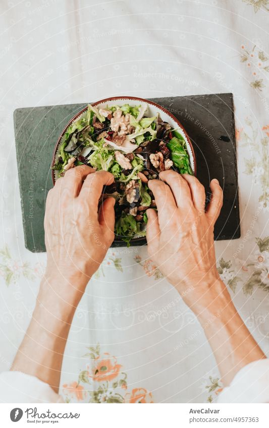 Grandma finishing a healthy recipe with wrinkled hands to upload it to networks.Salad with lettuce,nut,walnut,raisin and almond in a bowl on a black board.Perfect recipe for companion to diet