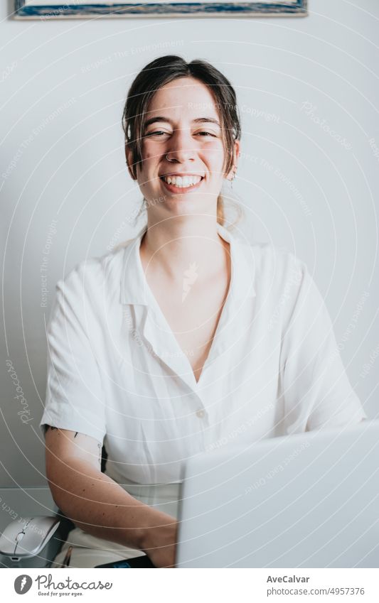 Portrait of young woman smiling at camera working on a laptop.Creative businesswoman consulting and revising documents.Enthusiastic and nervous with new job,office,coworkers,schedule,tasks and chores