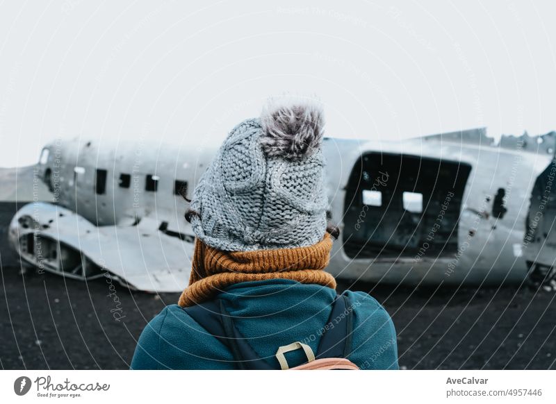 Woman on winter clothes in front of the wreck of th crashed airplane in Iceland, on the beach of Sólheimasandur. Travel to Iceland, road trip concept. Copy space image, visit Iceland.