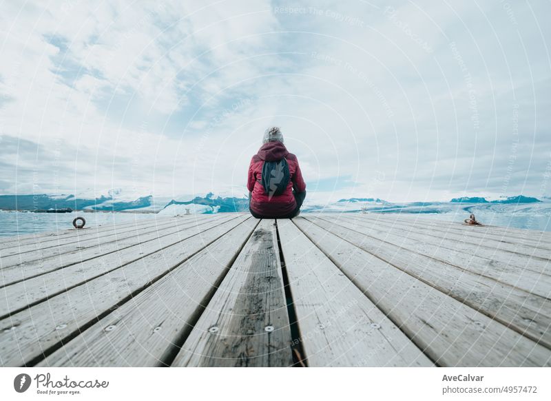 Young woman traveler back shot sitting on the docks relaxing and thinking in front of the glaciers of Jökulsárlón in Iceland. Copy space. Live your dream, love in Iceland, road trip style