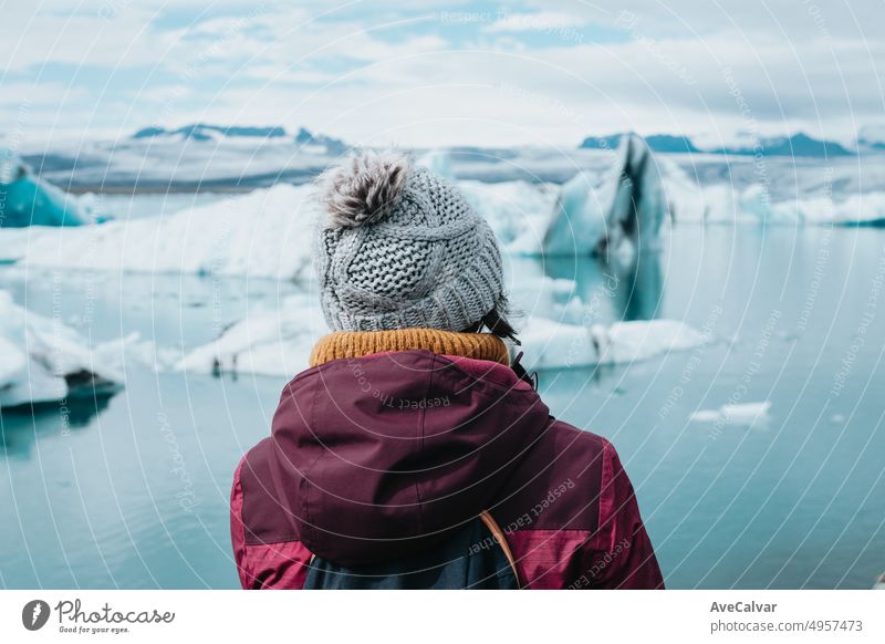 Traveler woman in cold weather clothes in front of the glaciers of Jökulsárlón in Iceland during a moody day filled with water. Live your dream, love in Iceland, road trip style.Copy space