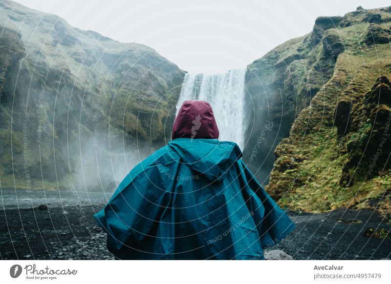 Woman on rain clothes in front of Skógafoss waterfall in Iceland during a moody day. Travel on van concept, road trip style. Visit Iceland and north countries concept.Copy space image