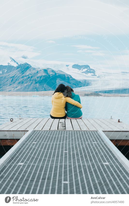 Couple of Young woman travelers back shot sitting on the docks relaxing and thinking in front of the glaciers of Jökulsárlón in Iceland. Copy space. Live your dream, love in Iceland, road trip style