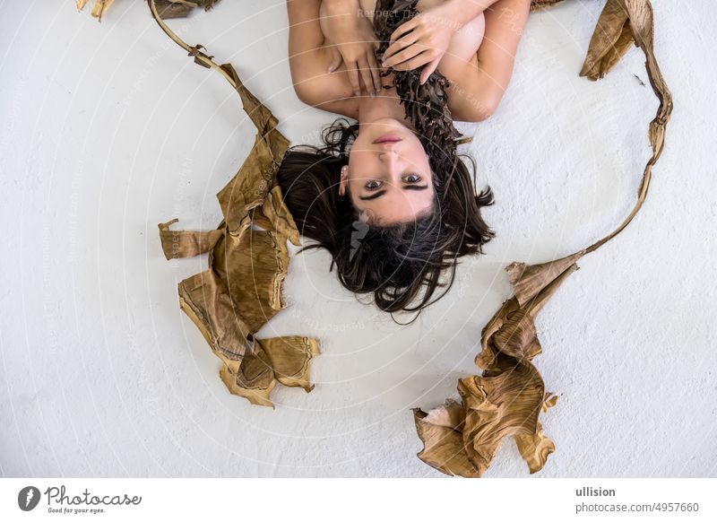 Portrait of a young sexy woman with brown hair artfully lying between leaves of dry decorative banana tree, upside down, copy space. portrait romantic natural