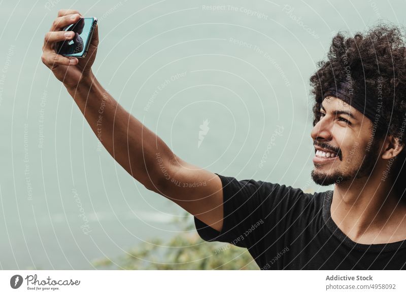 Cheerful black man taking selfie on smartphone against sea cheerful memory moment city afro using gadget device ethnic self portrait cellphone african american