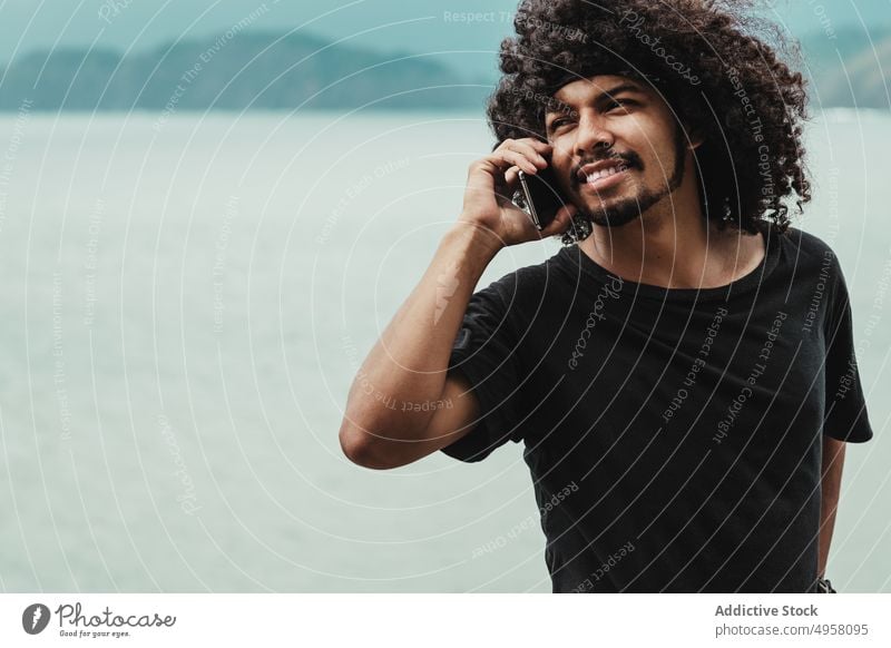 Black man having a phone call on smartphone against sea in town internet online pastime interested afro using gadget device cellphone hairstyle city speak
