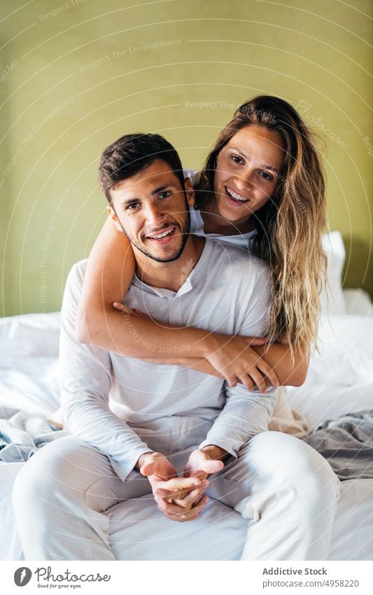 Smiling young woman hugging happy man from behind on bed couple embrace love affection bonding cheerful together tender fondness relationship cozy boyfriend