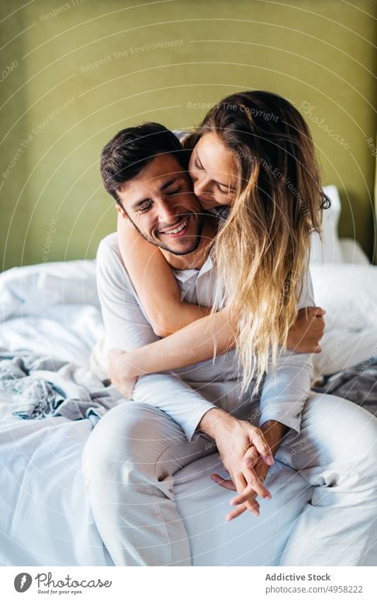 Smiling young woman hugging happy man from behind on bed couple embrace love affection bonding cheerful together tender fondness relationship cozy boyfriend