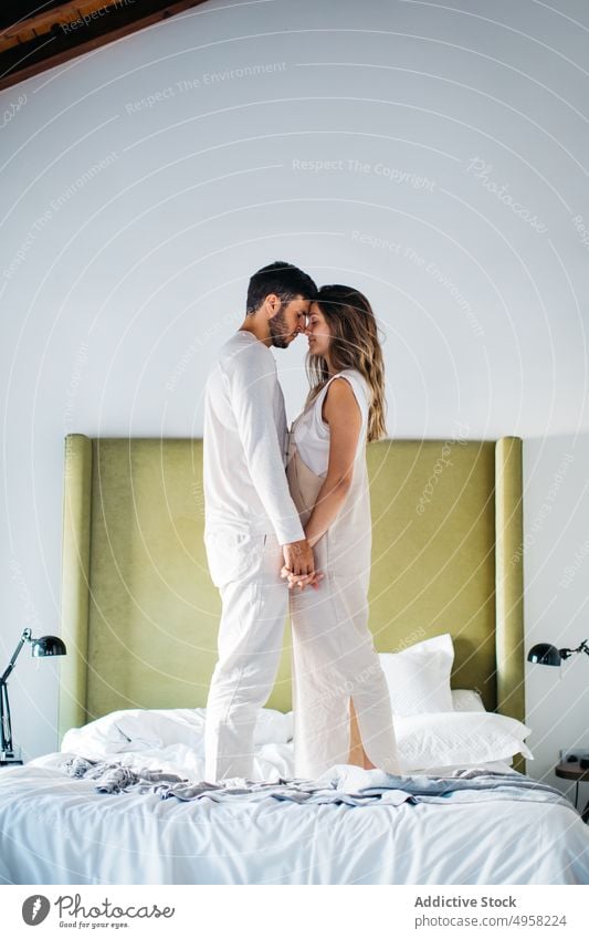 Delighted man and woman holding hands while standing on bed couple together affection romantic amorous fondness close relationship wife husband smile boyfriend