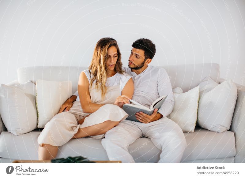 Young couple relaxing together on couch with book home bonding embrace happy domestic relationship love hug read affection sofa cheerful lifestyle smile