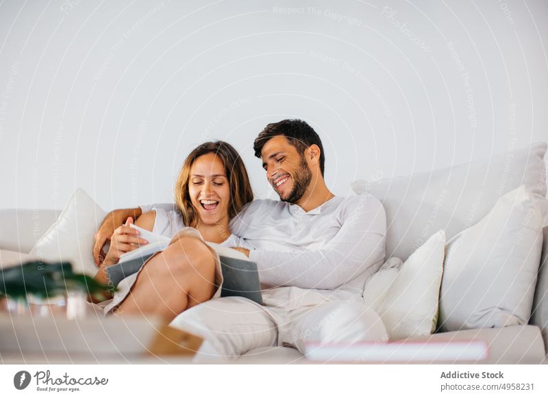 Young couple relaxing together on couch with book home bonding embrace happy domestic relationship love hug read affection sofa cheerful lifestyle smile
