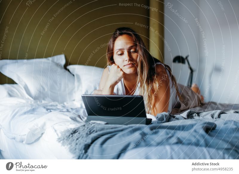 Young woman watching movie on tablet in bedroom using comfort device connection chill young female blanket soft lying gadget relax rest browsing modern home