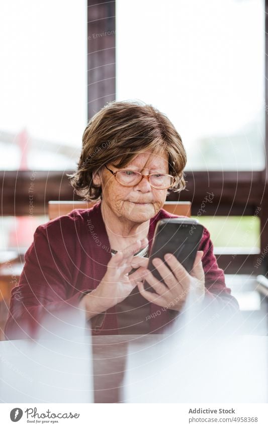 Elderly female using smartphone at table woman home elderly social media sit rest pensioner senior glasses browsing device gadget internet online connection