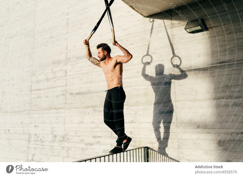 Athletic man balancing on gymnastic rings sportsman shirtless city athletic young active workout construction body lifestyle healthy male exercise fitness