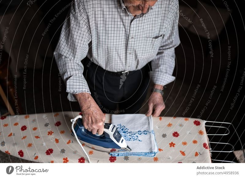 Anonymous elderly man ironing textile in room aged senior chore housework routine mature focus home male casual fabric domestic at home wrinkle couch process