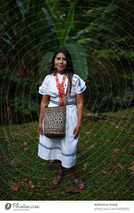 Smiling young native Arhuaco woman in forest indigenous portrait Colombia contemplative 20s nature Latin America traditional clothes necklace bag handmade craft