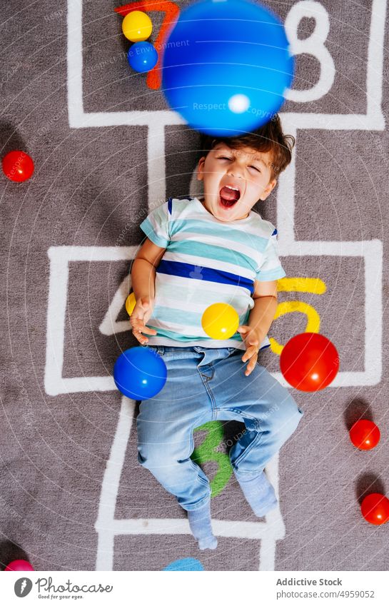 Happy boy playing with colorful balls throw home happy laugh casual floor activity game hopscotch excited kid fun number carpet toddler child toy amazed lying