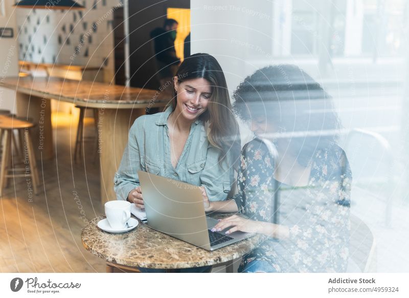 Smiling multiracial girlfriends sharing laptop in coffee shop best friend share smile internet online pastime women cafe using gadget weekend device glass wall