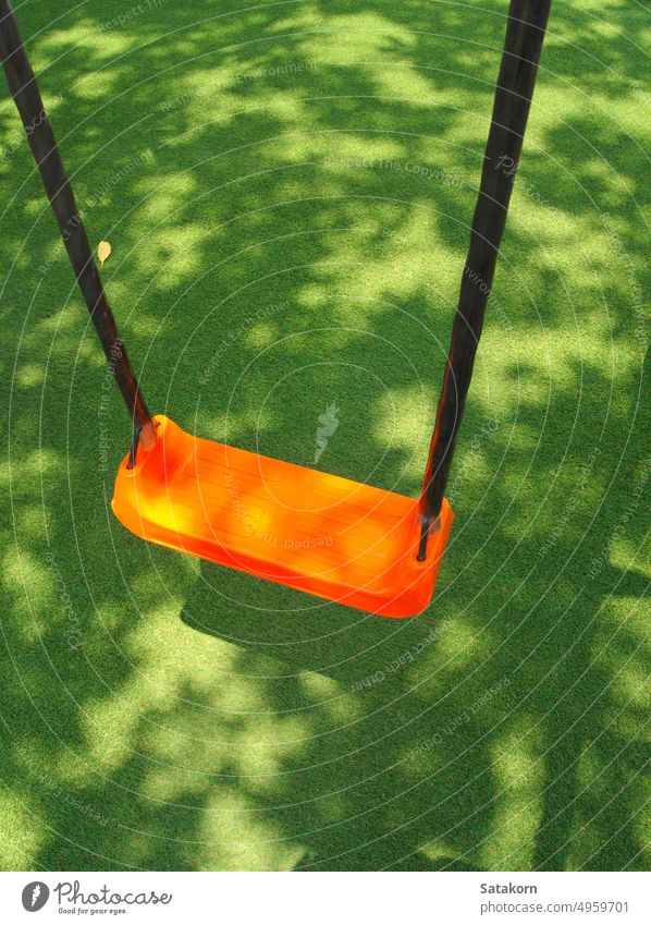 The orange color Swing seat on the artificial grass school yard playground swing child plastic park fun outdoor childhood recreation toy green colorful object