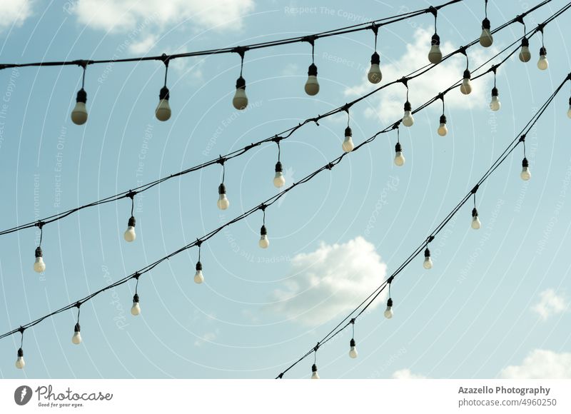 White economy light bulbs hanging in a row. Light bulbs view against the sky. air background blue blur bright cable cloud clouds cloudscape concept decoration