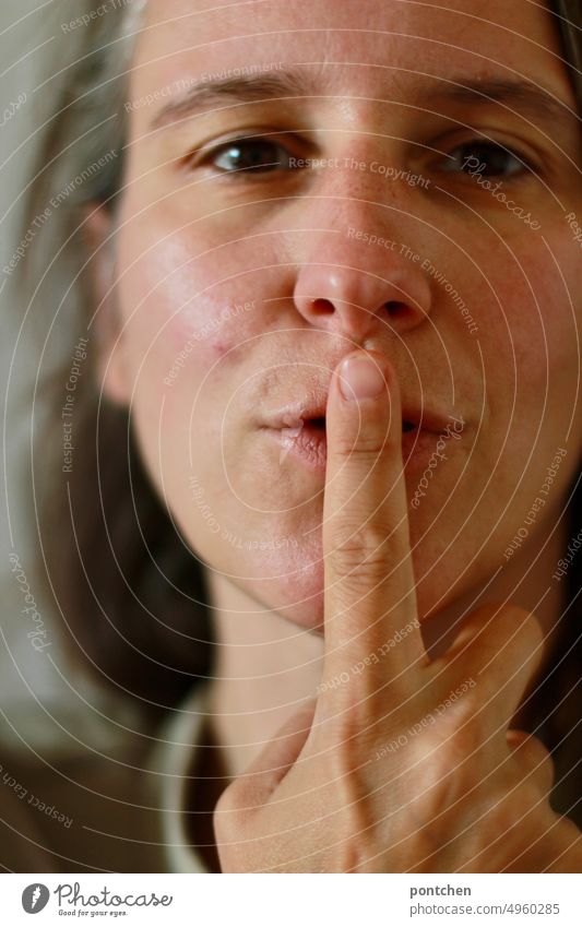 A woman puts her index finger over her mouth and asks for silence. Psst eye contact mystery tranquillity Forefinger Gestures Sign Fingers Interpret invitation