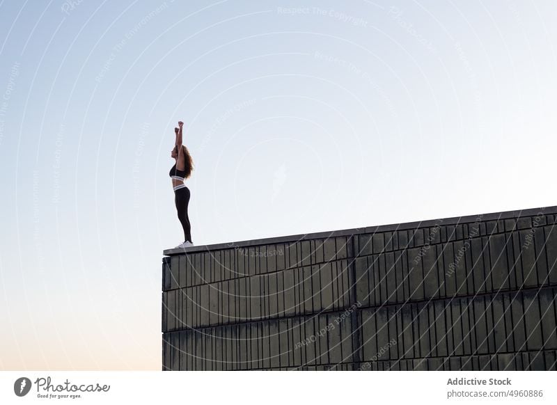Anonymous sportswoman with raised arms on roof under light sky sportswear arms raised freedom admire vitality energy sunset stand enjoy building wall