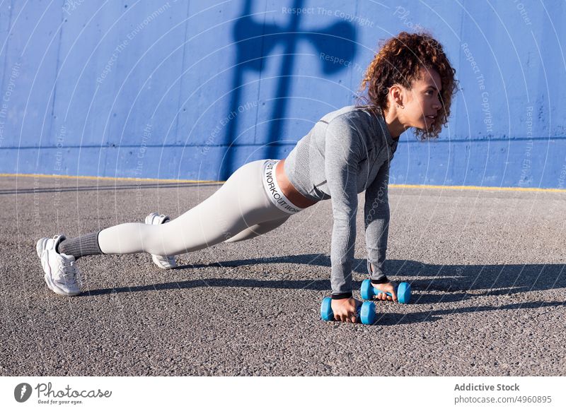 Determined sportswoman exercising with dumbbells on urban road plank endurance motivation strength training workout strong power confident weight equipment